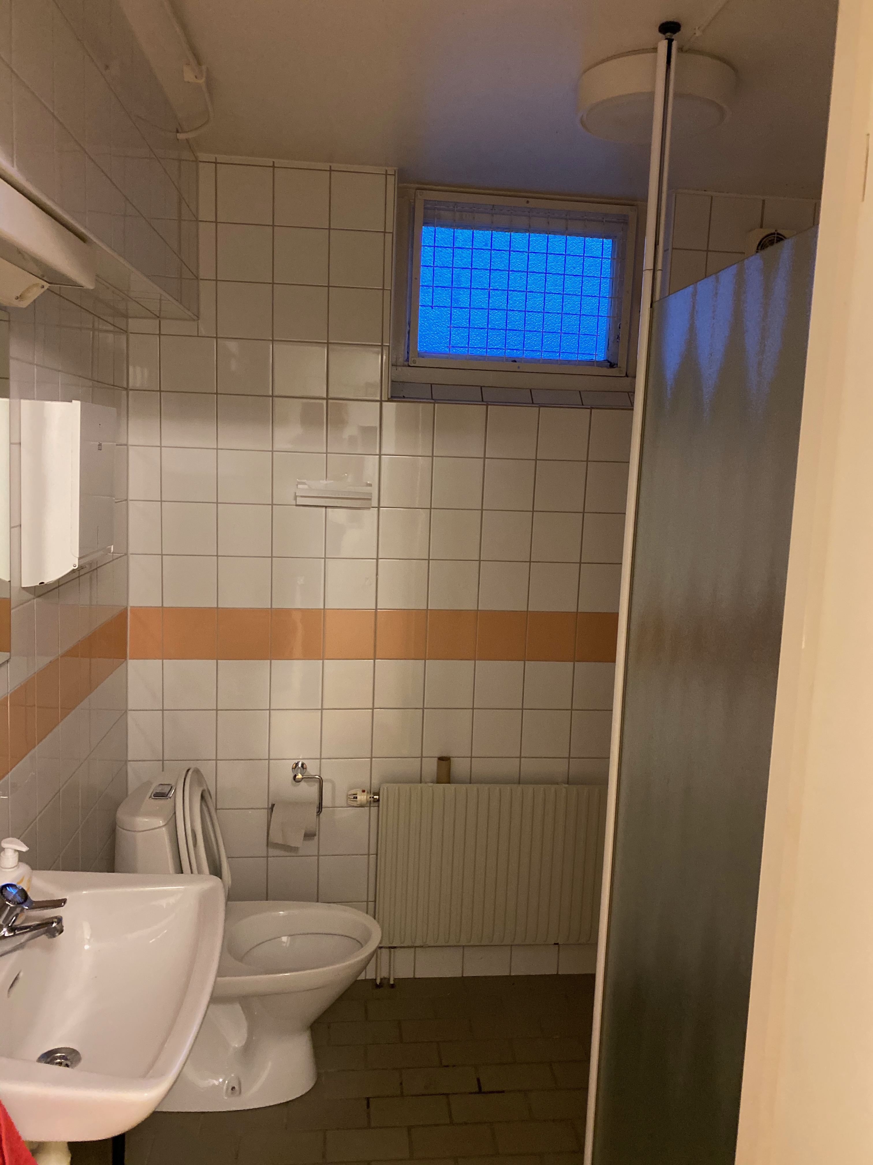 Gammalt badrum med orange kakelrand och dusch