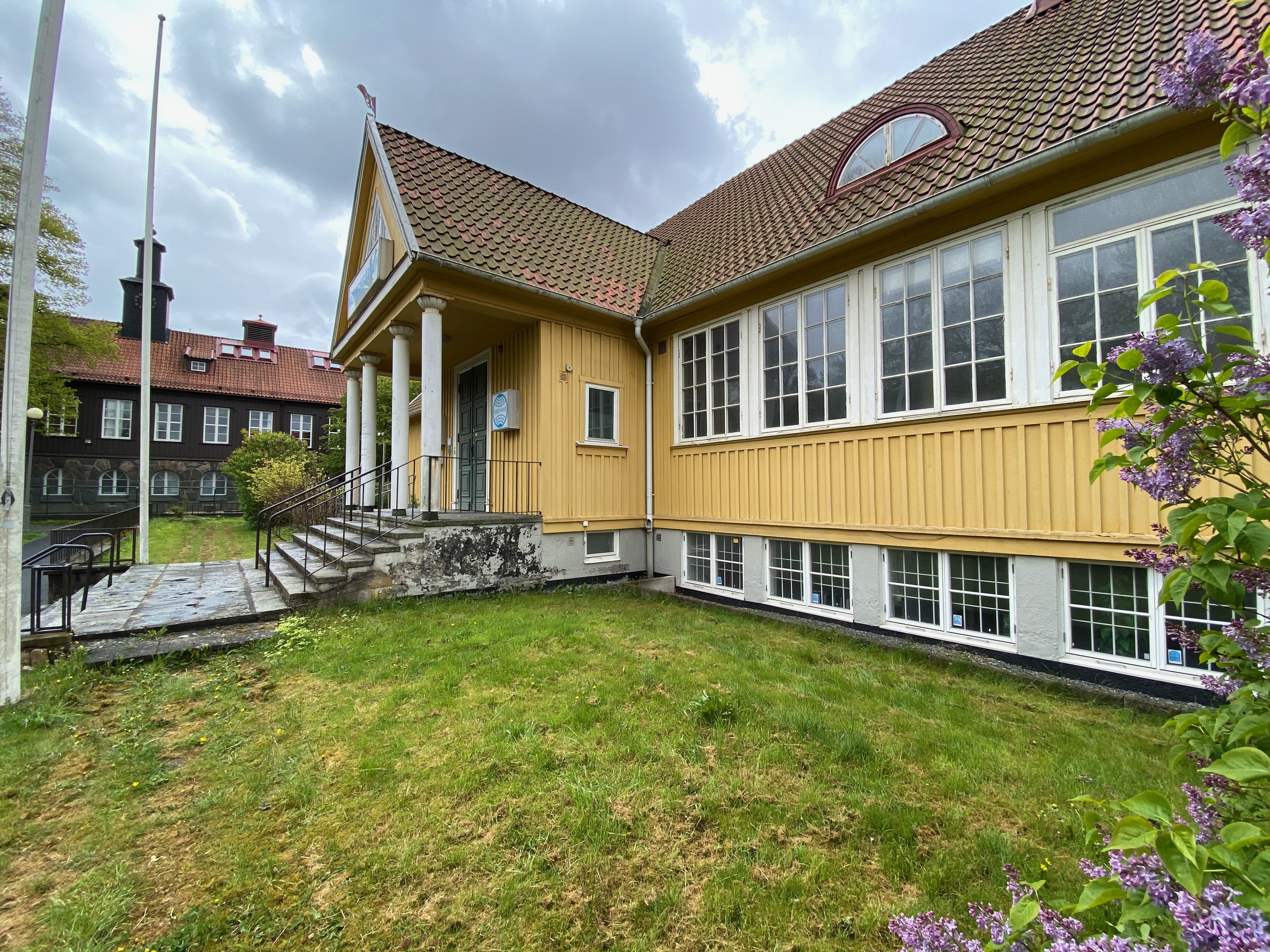 Entrén med portik, gräsmatta och blommande syrener