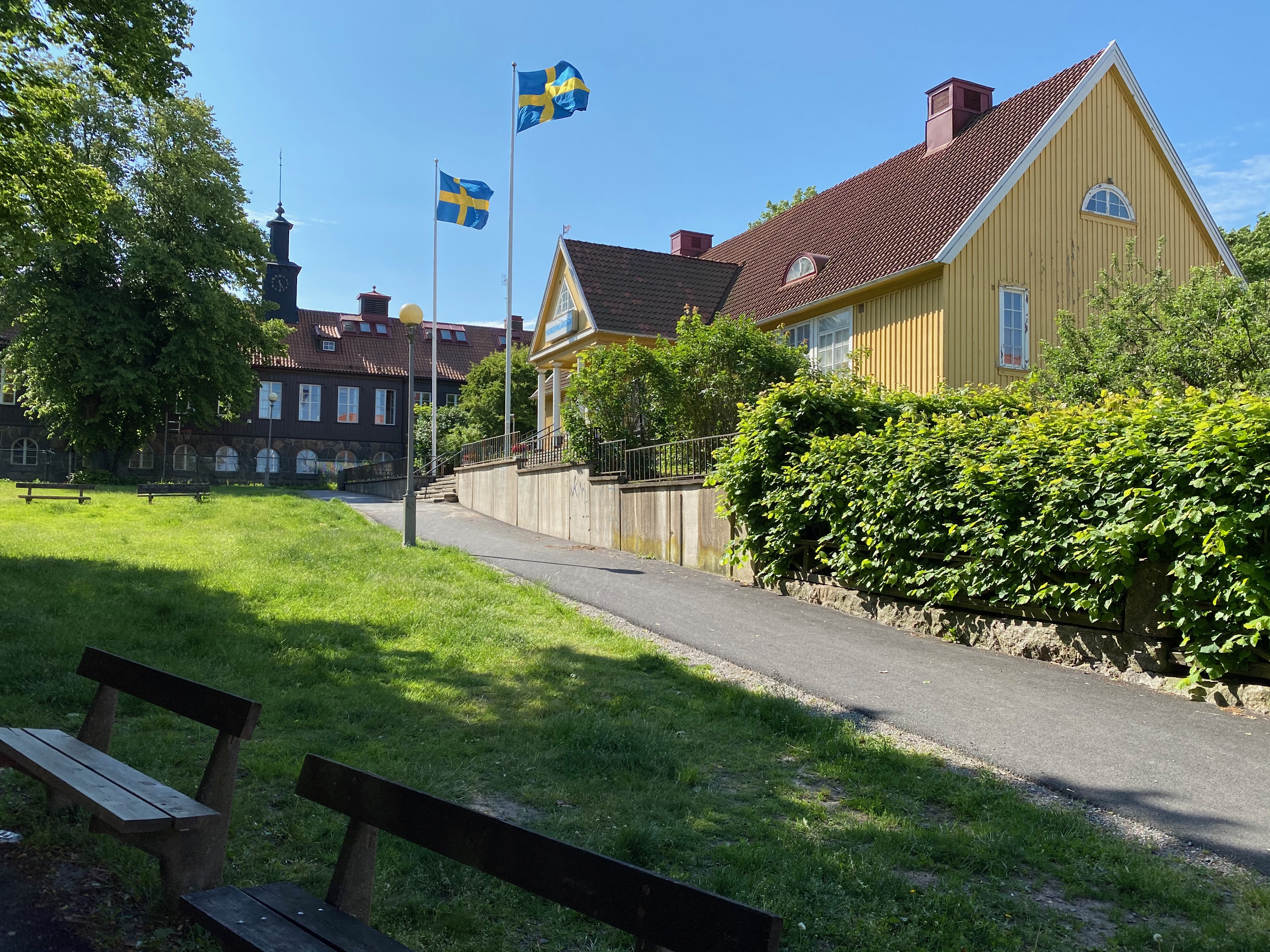 Sommarvy med svenska flaggor, gångväg och bänk